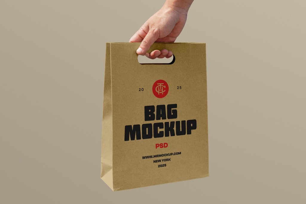 Front view, hand holding craft bag mockup with a strong red and black typography design against pastel yellow wall.