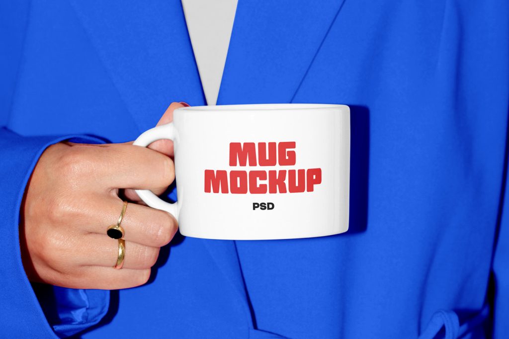 Front view, woman holding white mug mockup with strong red and black typography and in the background you can see her blue bathrobe.
