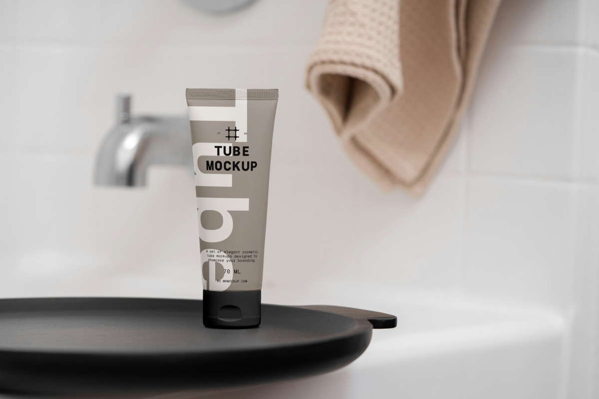 Front view, a Cosmetic Tube Mockup with delicate cosmetic design in black, white, and beige colors. Standing on the black tray. In the background you can see a brightly lit bathroom.
