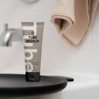 Front view, a Cosmetic Tube Mockup with delicate cosmetic design in black, white, and beige colors. Standing on the black tray. In the background you can see a brightly lit bathroom.