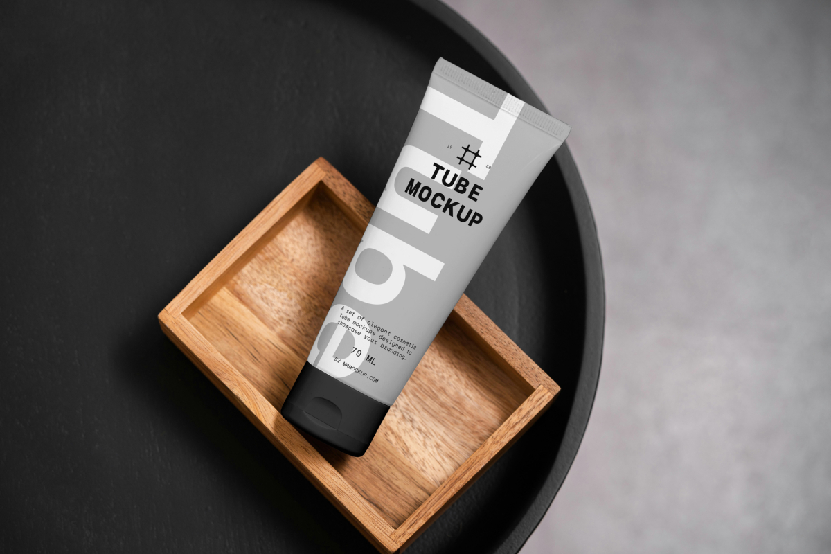View from above, a Cosmetic Tube Mockup with delicate cosmetic design in black, white, and gray colors, lying on a wooden box, which lies on a black tray.