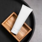 View from above, a white Cosmetic Tube Mockup lying on a wooden box, which lies on a black tray.
