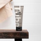 Front view, a Cosmetic Tube Mockup with delicate cosmetic design in black, cream, and beige colors, standing on a wooden stool, which is standing in the brightly lit bathroom.