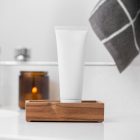 Front view, a white Cosmetic Tube Mockup standing in the wooden box, which lies on a white sink. In the background you can see a brightly lit bathroom.