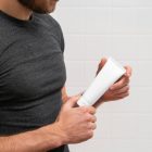 Front view, presents men holding a white Cosmetic Tube Mockups in both hands.