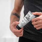Front view, close up view of men holding a Cosmetic Tube Mockups with delicate cosmetic design in black, white, and gray colors in both hands.