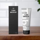 In the front view, a vertical Box Mockup and a Cosmetic Tube Mockup with delicate cosmetic designs in black, white, and gray colors stand next to each other on a wooden shelf in the bathroom.