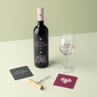 View from above, scene from Studio Wine Mockups of a standing black wine bottle with pink typography design, transparent wine glass with claret typography design, and two paper pads on the bright green background.