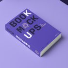 Top view at an angle of a softcover book mockup in PSD with bold typography design in black, gold, purple, and white colors showing the cover and spine in perspective view on the purple background.
