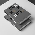 Top view at an angle of two hardcover book mockups in PSD with bold typography design in black, gold, gray, and white colors lying on top of each other for editorial and publishing design.