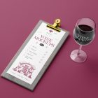 View from above, the scene from Studio Wine Mockups of a wooden menu with a typography design and a standing transparent wine glass with a typography design on the claret background.