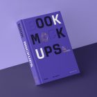 Front view, a hardcover book mockup with bold typography design in black, gold, purple, and white colors leaning against the purple wall, standing in perspective on the dark purple background.