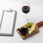 View from above, scene from Studio Wine Mockups wooden menu, standing transparent wine glass, and lying wooden tray with camembert and grapes on the white background.