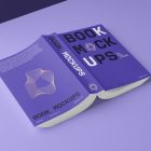 View from above, a softcover book mockup turned upside down with bold typography design in black, gold, purple, and white colors lying on the purple background in perspective view.