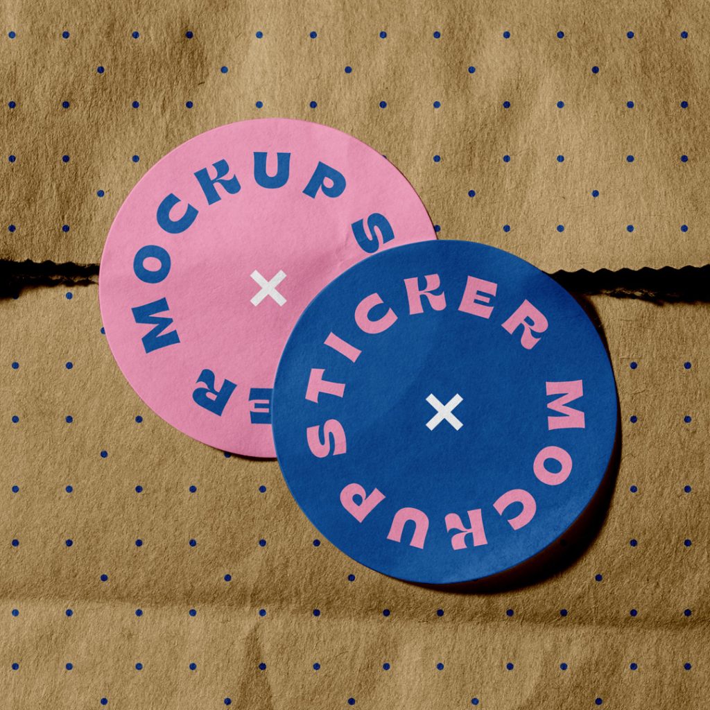 View from above, two rounded Sticker Mockup with slab typography design in pink and navy blue colors are glued to the craft paper bag.