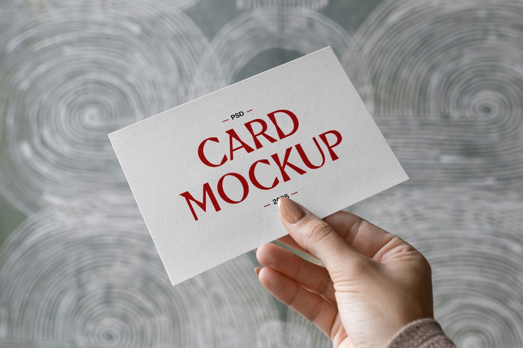 Front view, hand holding card mockup with red and black typography design against the wall.