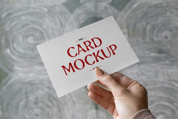 Front view, hand holding card mockup with red and black typography design against the wall.