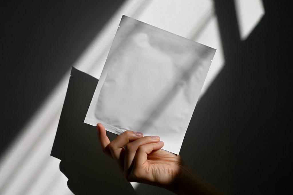 Front view, hand holding white bag mockup against the white wall with shadows.