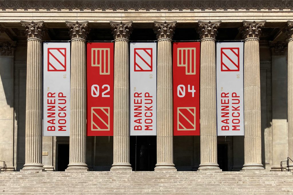 Front view, five vertical mockups with white, red, and cream geometric designs hanging between the columns on the facade of the building just above the entrance to the museum.