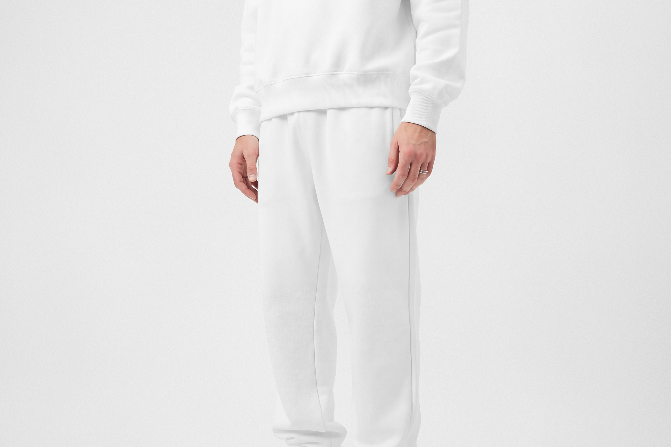 Front view of a standing male model wearing white sweatpants & a white sweatshirt mockup against a white studio background from the studio apparel mockups product.