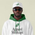 Front view, Black male model wearing a white cap & a white hoodie mockup with typography design standing against the bright studio background from the studio apparel mockups product.