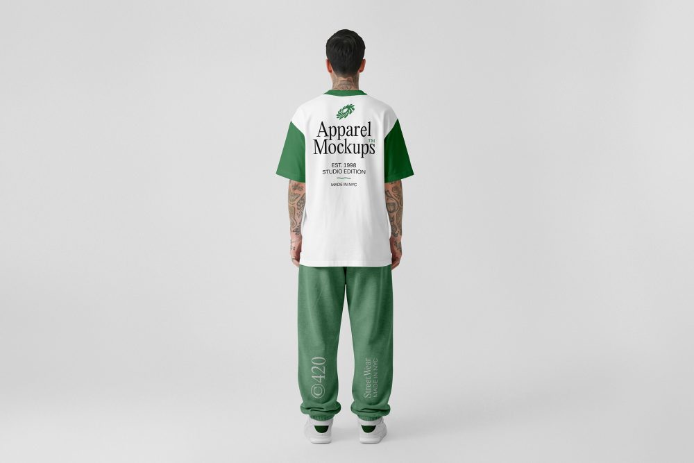 Front view, male model standing backward wearing a white t-shirt & a pastel green sweatpants mockup with typography design against a grey studio background from the studio apparel mockups product.