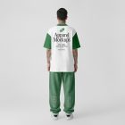 Front view, male model standing backward wearing a white t-shirt & a pastel green sweatpants mockup with typography design against a grey studio background from the studio apparel mockups product.