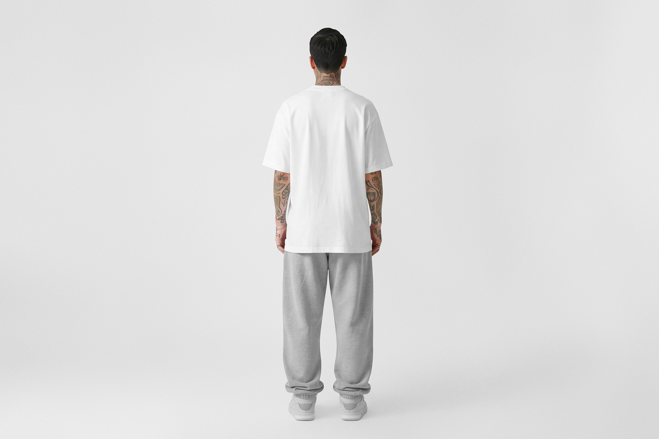 Front view, male model standing backward wearing a white t-shirt & grey sweatpants mockup against a white studio background from the studio apparel mockups product.