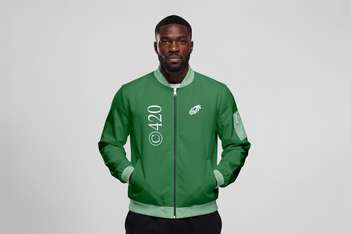 Front view, Black male model wearing a green jacket mockup with a white typography design standing against the grey studio background from the studio apparel mockups product.