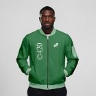 Front view, Black male model wearing a green jacket mockup with a white typography design standing against the grey studio background from the studio apparel mockups product.