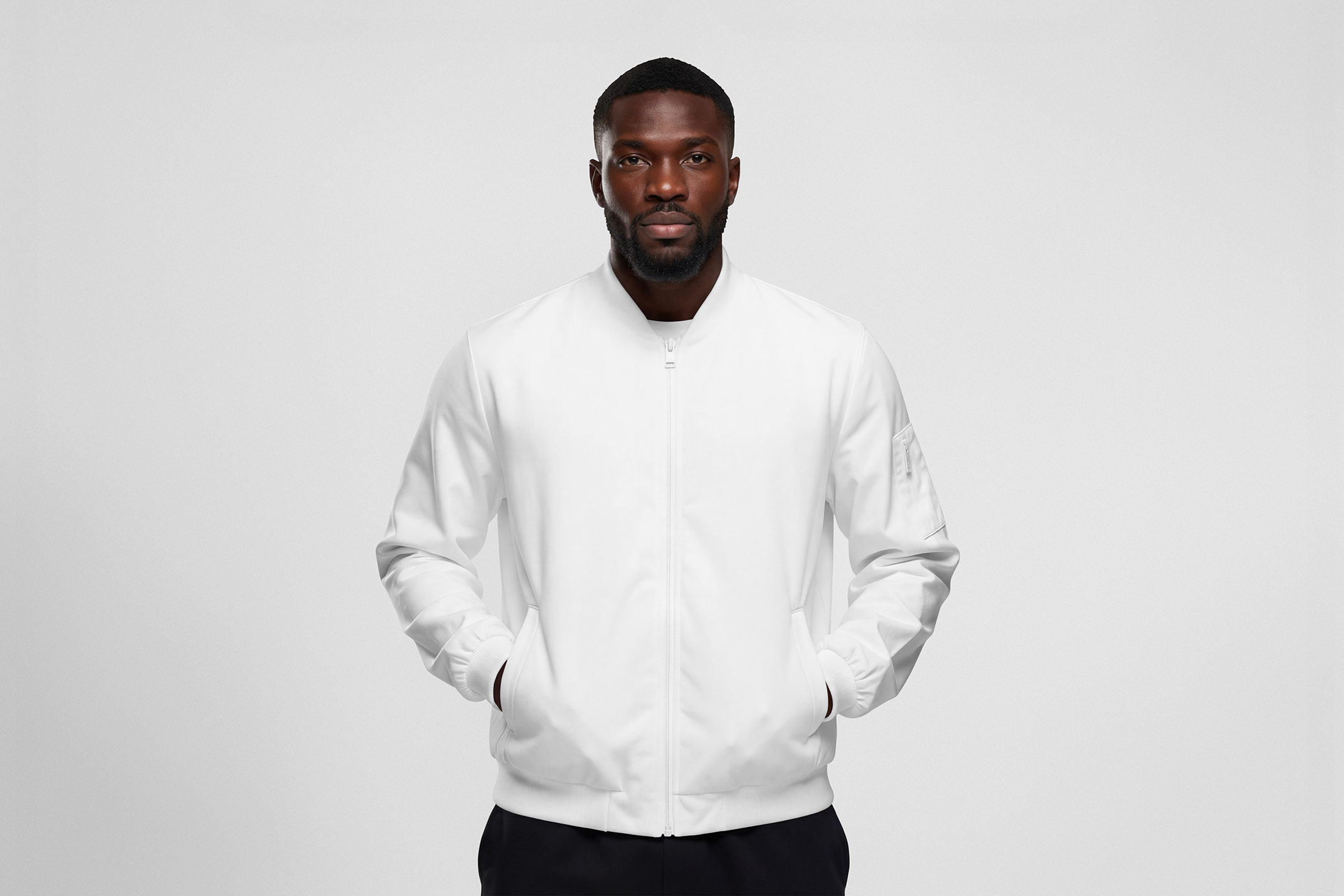Front view, Black male model wearing a white jacket mockup standing against the white studio background from the studio apparel mockups product.