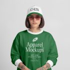 Front view of a female model wearing a green sweatshirt and white cap mockup with a white and black typography design standing against the grey studio background from the studio apparel mockups product.