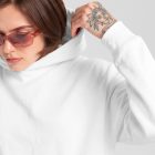 Front view of a female model wearing a white hoodie mockup standing against the white studio background from the studio apparel mockups product.