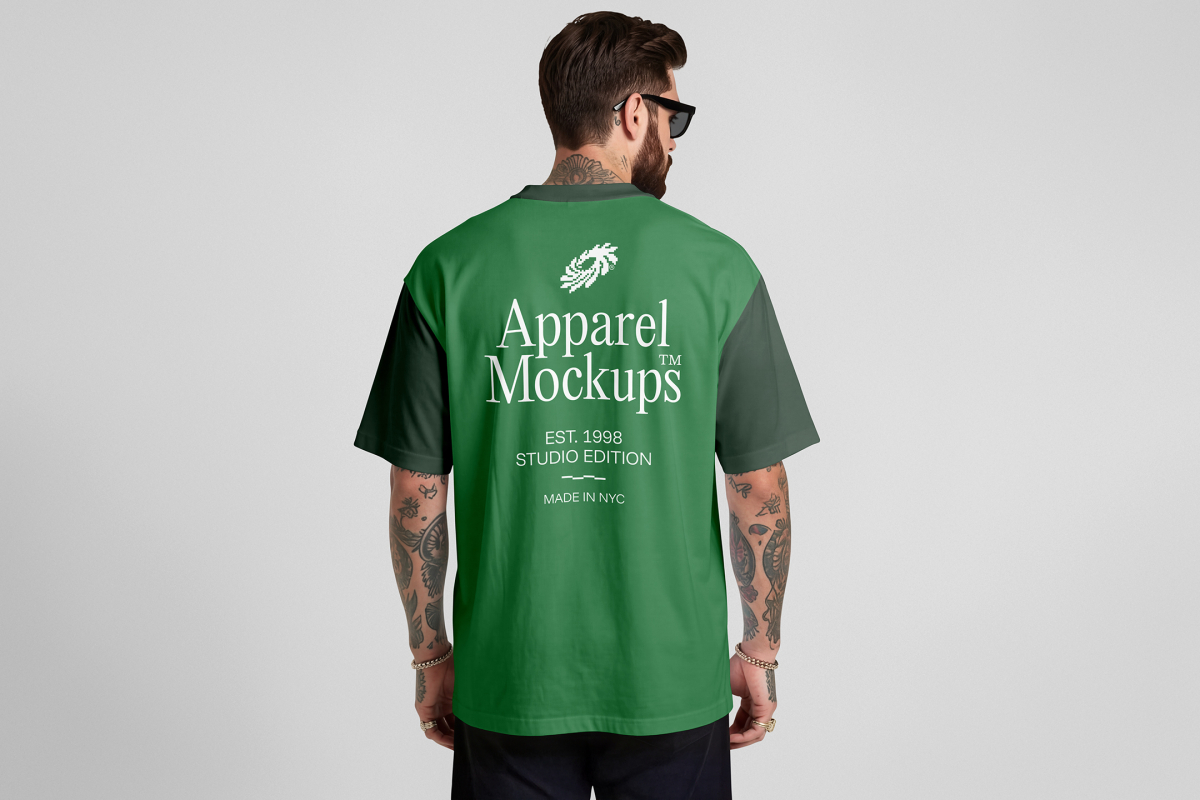 Front view, male model backward wearing a green t-shirt mockup with white typography design standing against a grey studio background from the studio apparel mockups product.