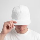 Front view of a male model wearing a white five panel cap mockup held by hand, standing against the white studio background from the studio apparel mockups product.
