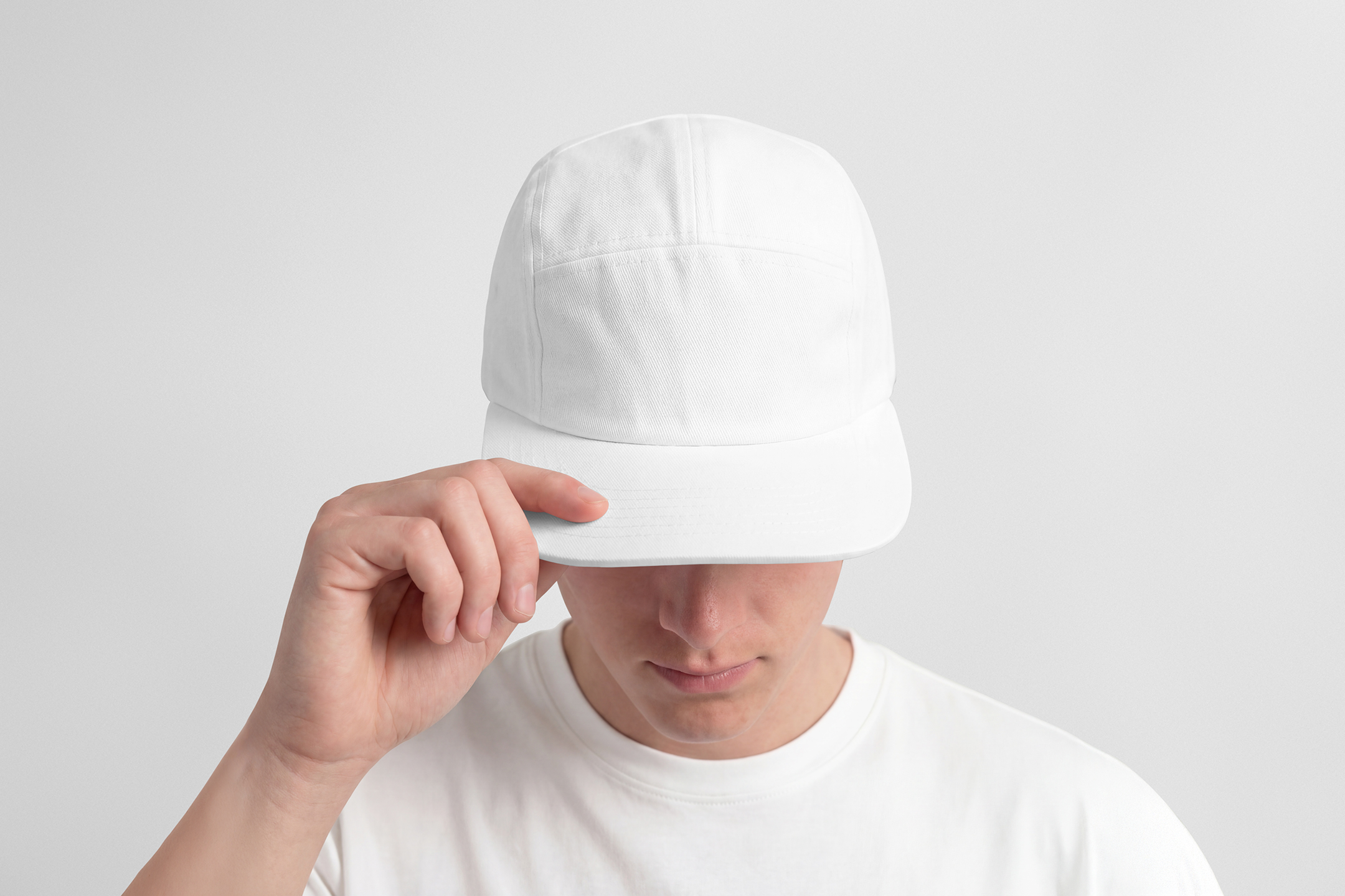 Front view of a male model wearing a white five panel cap mockup held by hand, standing against the white studio background from the studio apparel mockups product.