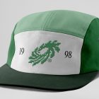 Front view, lying five panel cap mockup in three shades of green and white colors with black typography design and green logo on the grey studio background from the studio apparel mockups product.