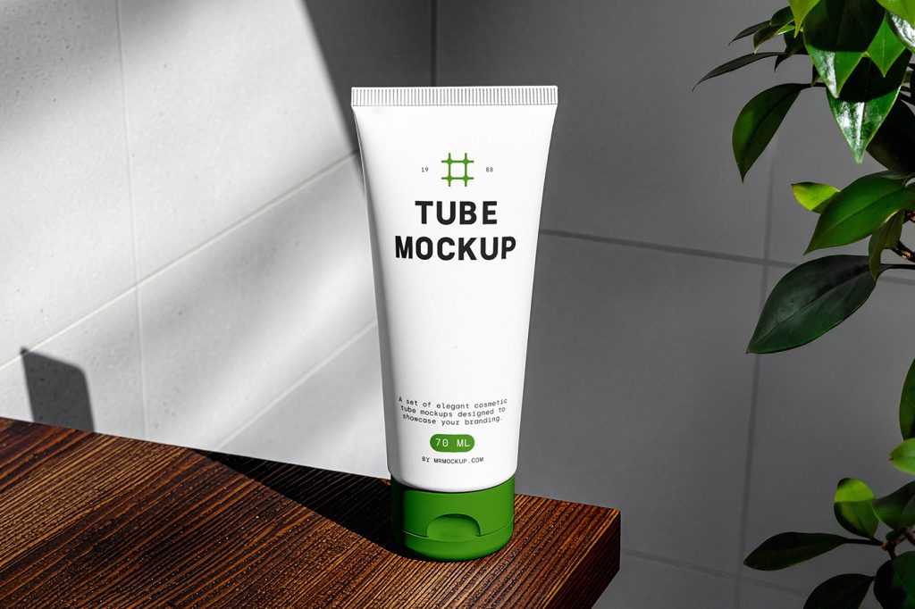 Front view of a white, minimalistic cosmetic tube mockup with a green lid standing on the wood in a bathroom.