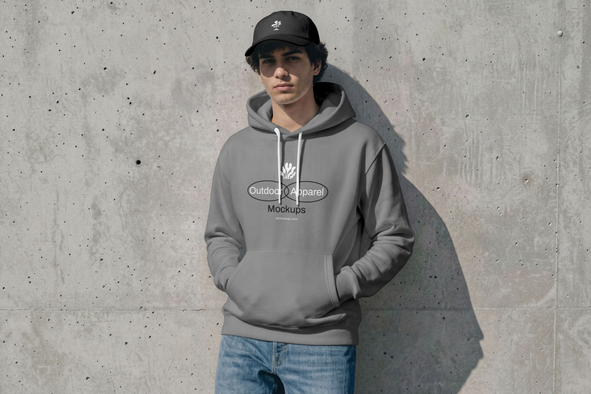 Male model resists on concrete wall wearing hoodie mockup in gray color with simple geometric typography logo and black cap mockup from the Outdoor Apparel Mockups Vol.3 product.