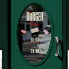 A close-up of a dark green restaurant door featuring an oval glass window. The glass shows brand decals, mockup stickers, and opening hours listed as open 10:00 and close 20:00.
