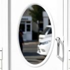 A close-up of a white restaurant entrance door featuring a vertical oval glass window and a silver handle. The street outside is reflected in the window pane.