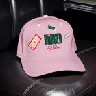 A close-up shot of a light pink baseball cap resting on a dark, quilted leather booth inside a restaurant. The front of the cap features a green "BÜRGER" brand logo with red stickers that say "MOCKUP".