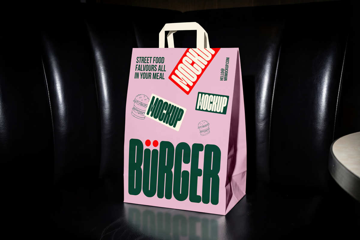 A pink paper shopping bag with white handles placed on a black leather booth inside a restaurant. The bag features a prominent dark green "BÜRGER" logo, burger illustrations, and a bold red "MOCKUP" sticker.