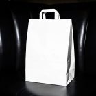 A blank white paper shopping bag with flat handles, standing upright on a black leather booth seat inside a dimly lit restaurant.
