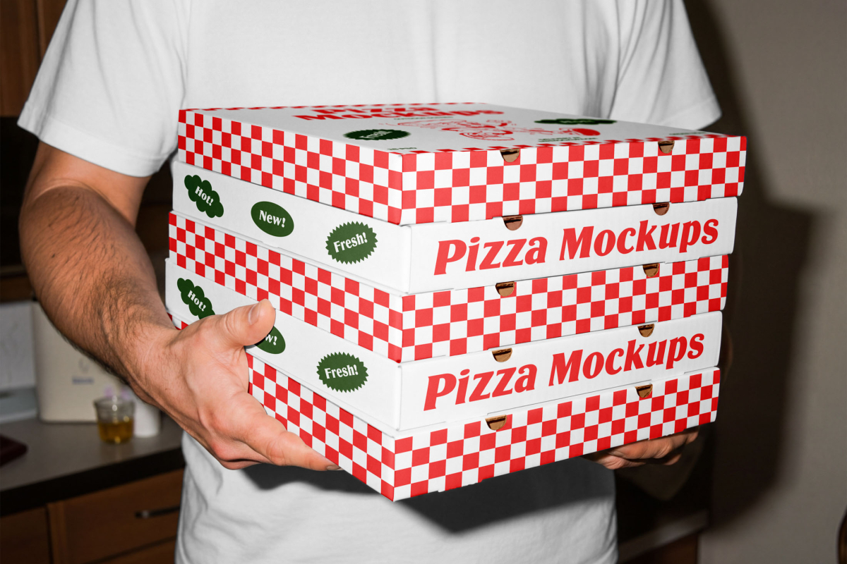 A person holding a stack of five white pizza boxes with red checkered side borders. The sides of the boxes prominently display the red "Pizza Mockups" text alongside green badges reading "Hot!", "New!", and "Fresh!".