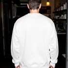 The back view of a man wearing a blank white sweatshirt, standing in a dimly lit restaurant corridor with exposed brick walls.