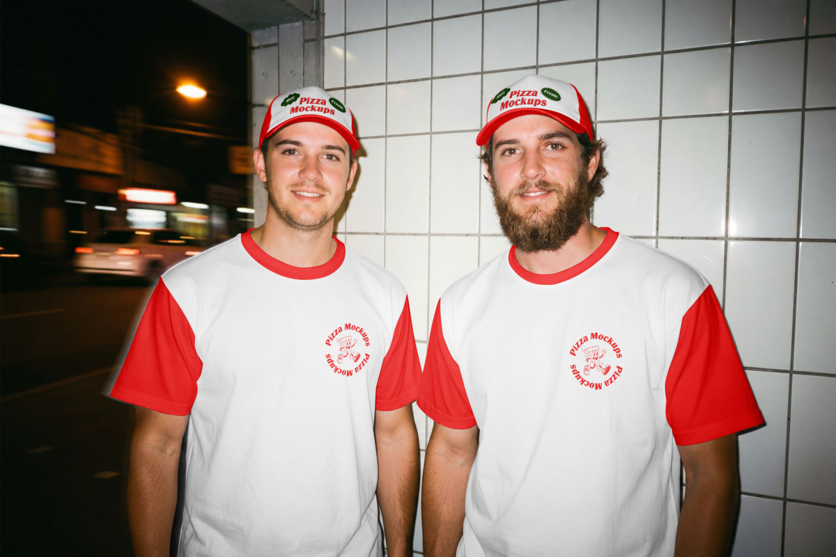 Two young men standing side-by-side against a white tiled wall. Both are wearing white ringer t-shirts with red sleeves and a red circular "Pizza Mockups" logo, along with matching red and white trucker hats.