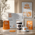 A complete coffee shop branding mockup set displayed on a round marble table, including a bi-fold menu, paper coffee cup, ceramic espresso cup, table tent, and framed wall poster.