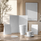 A collection of blank white coffee branding mockups, including a menu, paper coffee cup, espresso cup and saucer, and table tents on a round stone table.