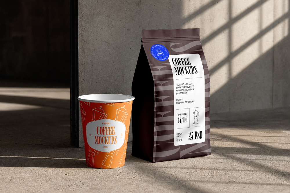 An orange takeaway paper coffee cup standing next to a dark brown coffee bag on a concrete floor with sunlight casting window shadows.